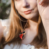 A woman in a white blouse holds up an anatomical heart necklace, the gold pendant in sharp focus while her face remains softly blurred, highlighting this piece of unique jewelry.