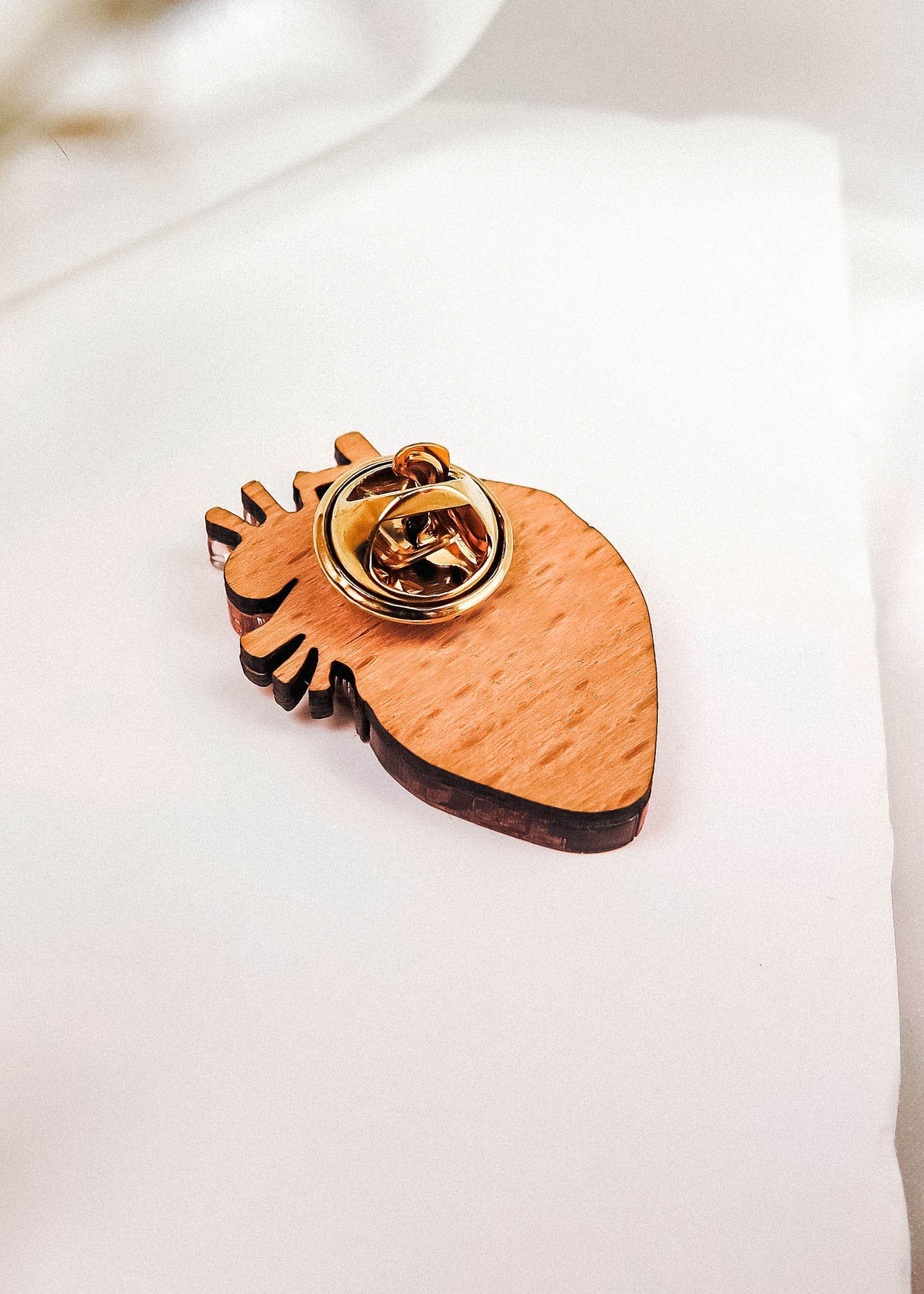 A handcrafted wooden keychain shaped like an anatomical heart with a gold metal key ring attached, resting on a white fabric background—a true statement piece for any collection.
