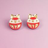 A pair of round, festive earrings with gold bows and accents, red details, and white background, perfect as holiday jewelry. Displayed on a light purple surface, these Poinsettia Statement Hoops add a cheerful touch to any celebration.