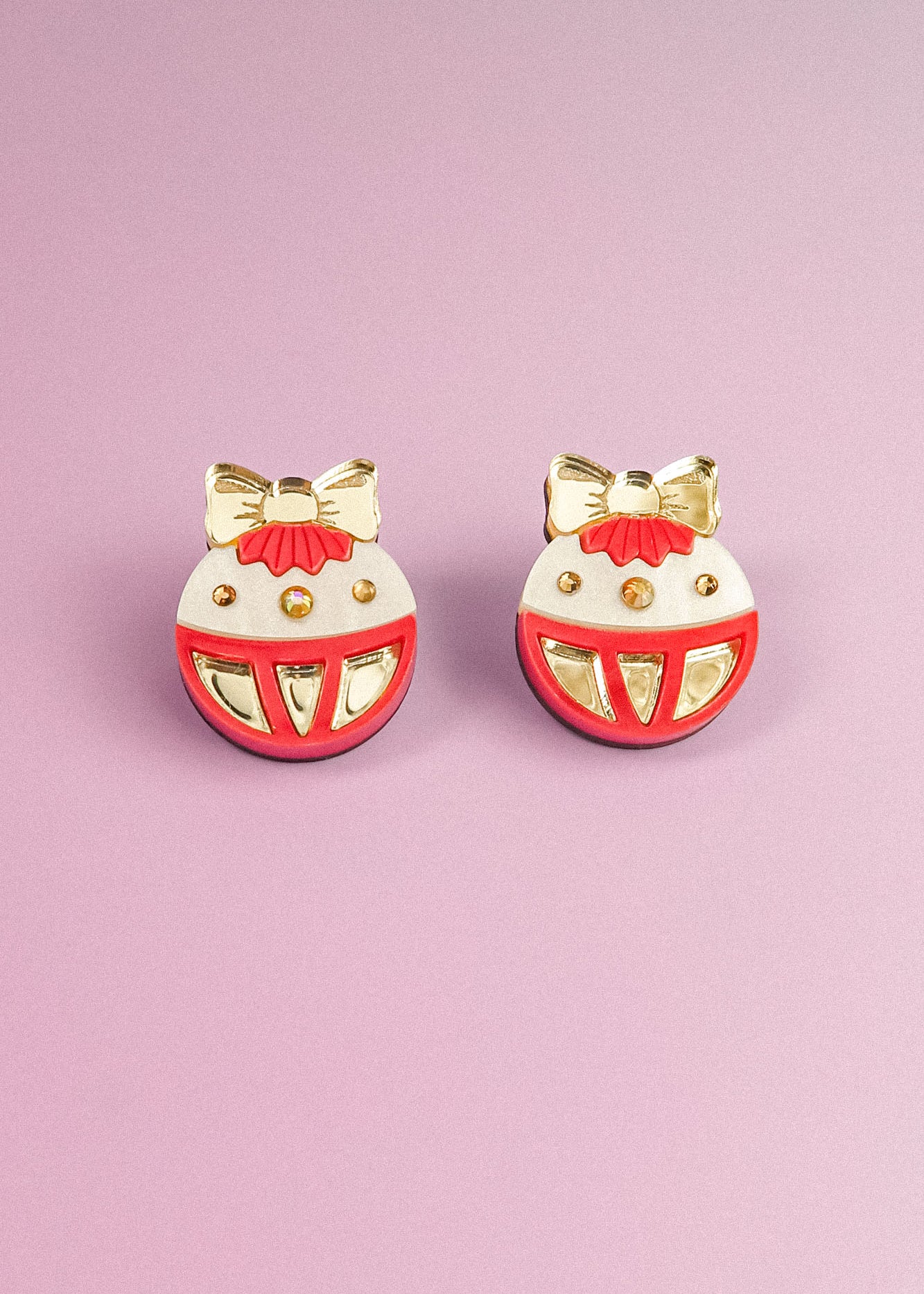 A pair of round, festive earrings with gold bows and accents, red details, and white background, perfect as holiday jewelry. Displayed on a light purple surface, these Poinsettia Statement Hoops add a cheerful touch to any celebration.