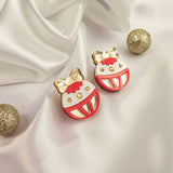 Two round, decorative festive earrings with red, white, and gold details, featuring bows and smiling faces, are placed on white satin fabric amid three glittery gold spheres—perfect as holiday jewelry or Poinsettia Statement Hoops.