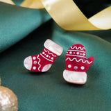 A festive holiday earrings set featuring Christmas Knitted Studs—a red mitten and red sock with white details and rhinestones—displayed on green fabric with a gold satin ribbon in the background.
