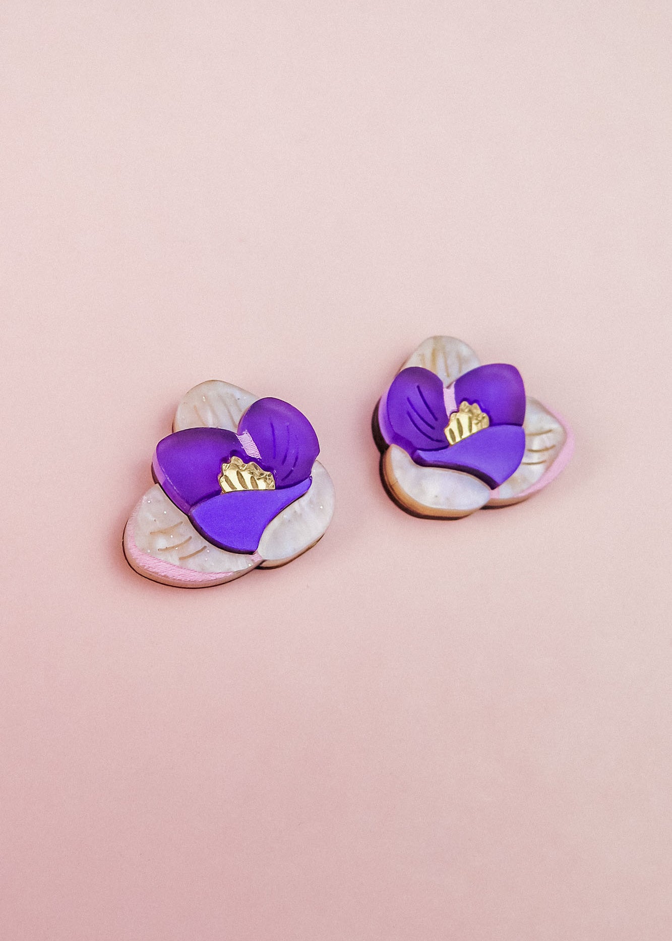 Crocus Stud Earrings shaped like purple flowers with yellow centers, set against a light pink background. The petals are layered, hand-painted flowers with a delicate, handmade appearance and are allergy-free.