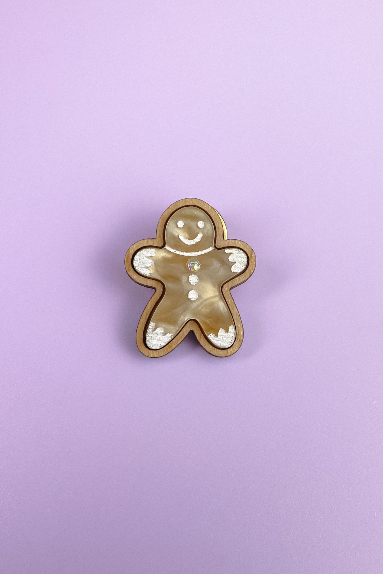A Gingerbread Man Pin brooch with a smiling face and decorative white icing details, set against a solid light purple background—perfect for adding a festive touch to your Christmas party outfit.