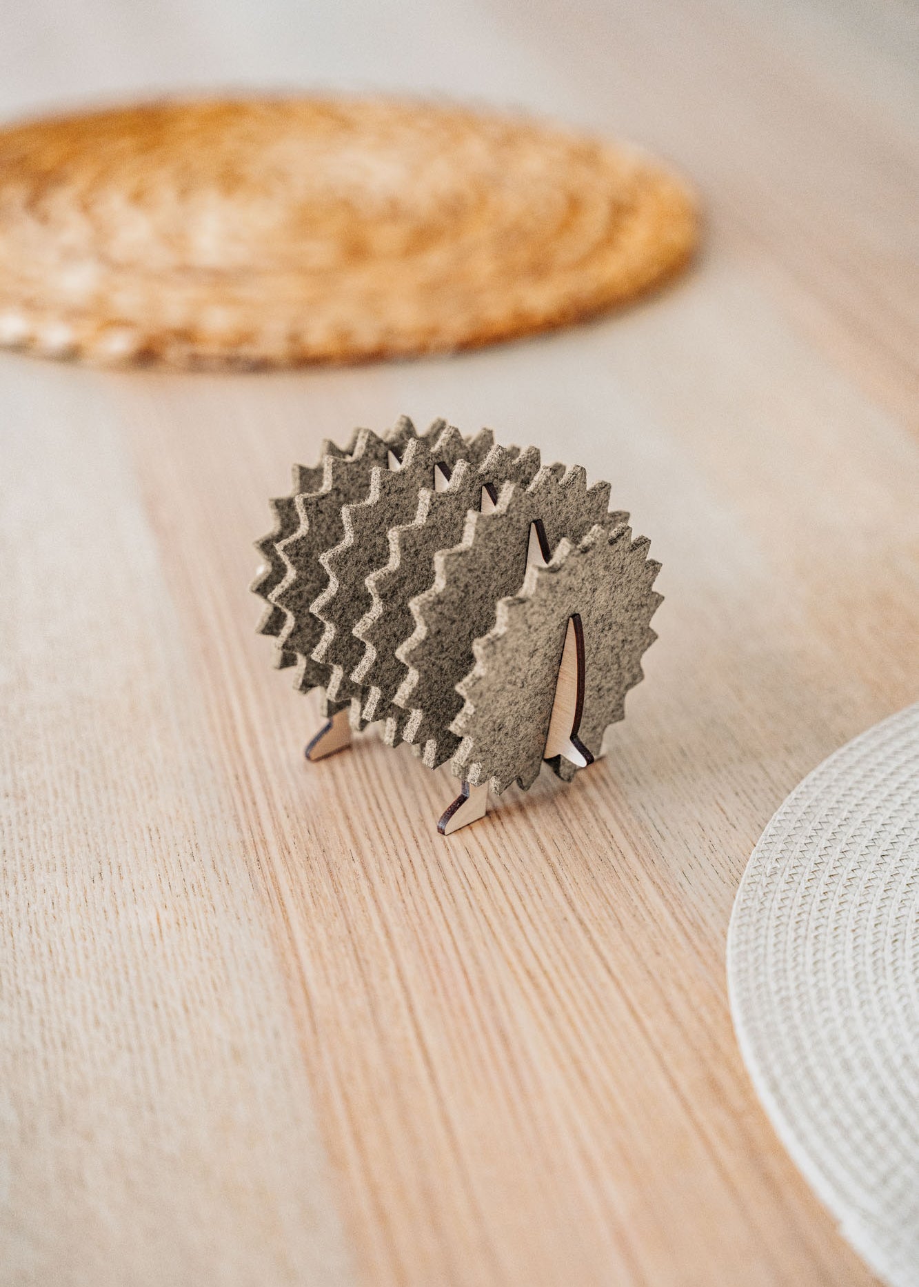 A small, decorative wooden hedgehog coaster holder made of felt and plywood sits on a wooden table, adding charm to your home decor, with woven placemats in the background.