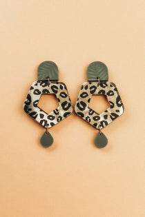 A pair of Leopard Earrings with olive green tops and teardrop-shaped dangles, featuring hexagonal centers in timeless patterns, crafted from premium materials and displayed on a peach background.