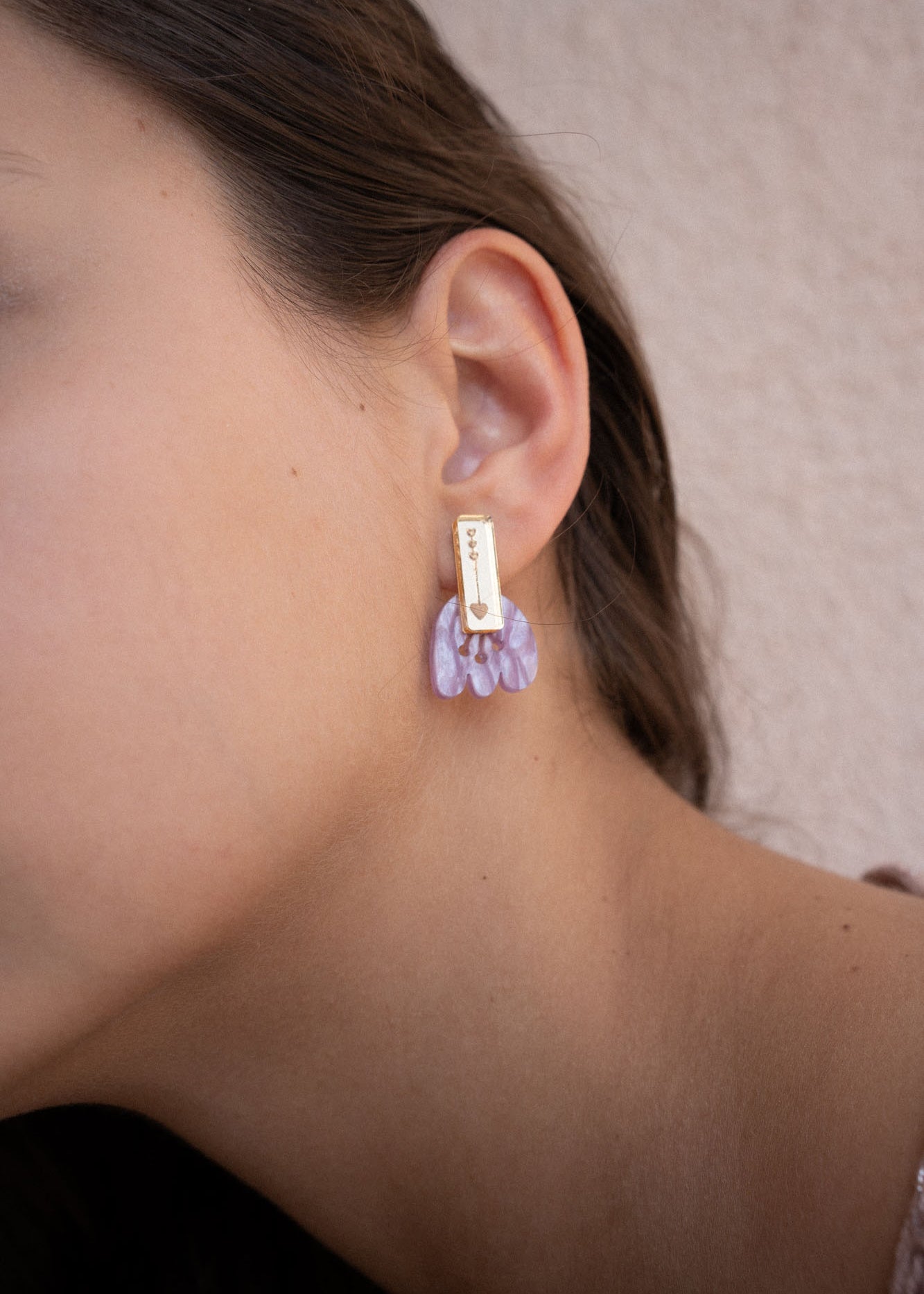 Close-up of a person wearing a gold rectangular earring with marbled purple acrylic petal-shaped accents, against a light beige background. Showcased on the left ear, these Romantic Tulip Earrings offer allergy-free comfort.