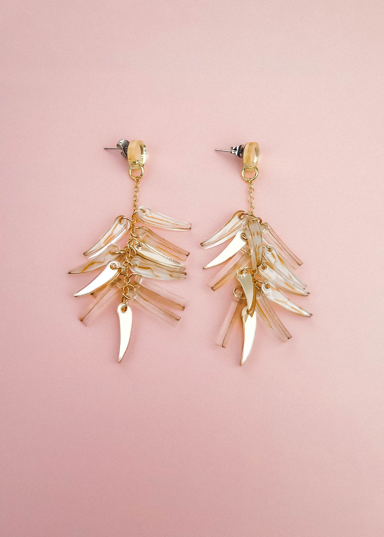 A pair of gold and clear featherlight dangle earrings with multiple dangling, leaf-shaped charms arranged in layered clusters, displayed on a soft pink background.
