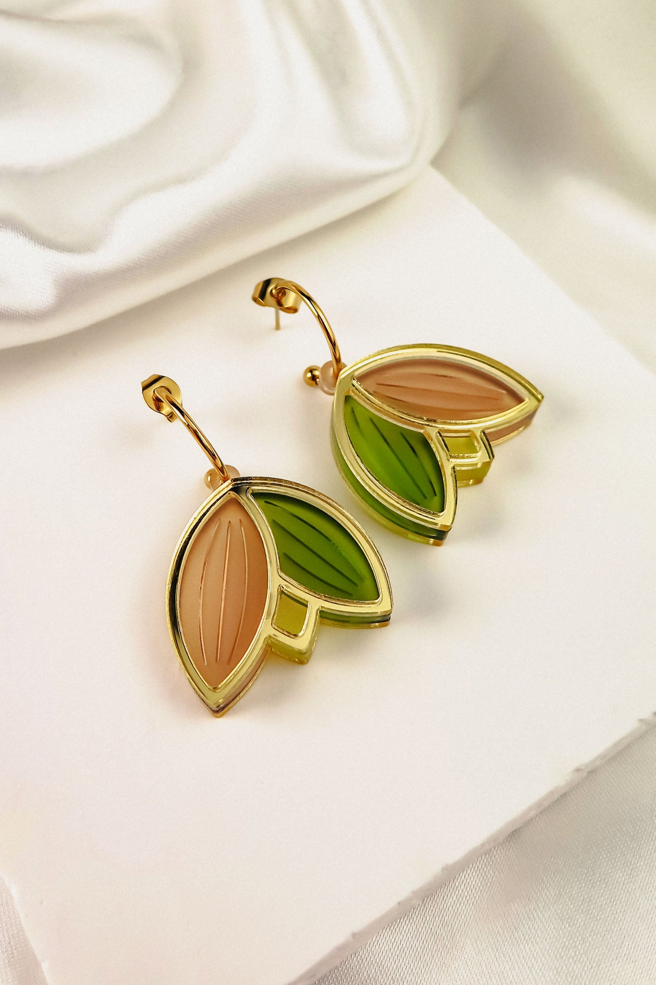 Gold Tulip Huggie Earrings with a leaf design, featuring cream, green, and taupe enamel sections. These lightweight, handcrafted earrings are displayed on a white surface with soft, white satin in the background.